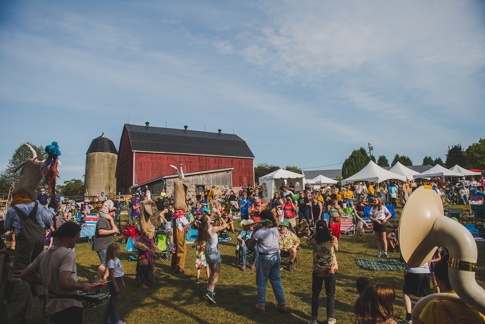 It is a sunny day at Haute Goat farm, crowd of festival attendees is watching a band play music on a grassy field. This image illustrates the vibe at Cultivate Festival in 2025.