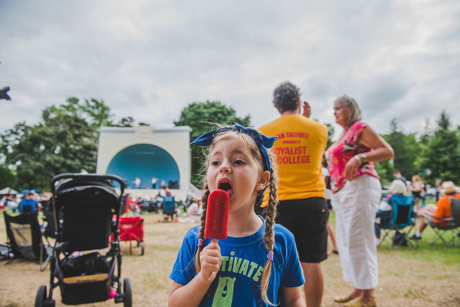 Young girl liking a popsicle at Road to Cultivate under a scattered cloud sky in front of the historic bandshell